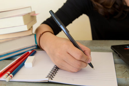 Young woman working, doing homework, with notebook and laptop, closeup on hand