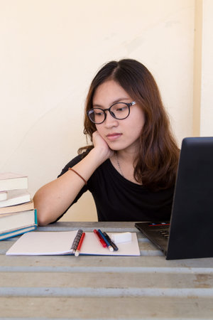 Young woman tired of working, doing homework, with notebook and laptop