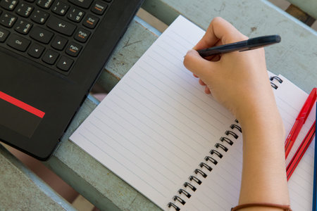 Young woman working, doing homework, with notebook and laptop, closeup on hand