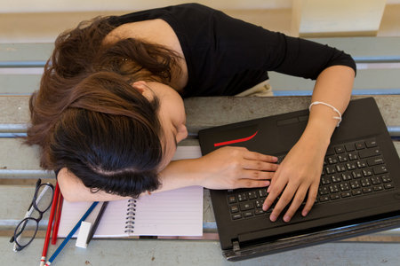 Young woman tired of working, doing homework, with notebook and laptop