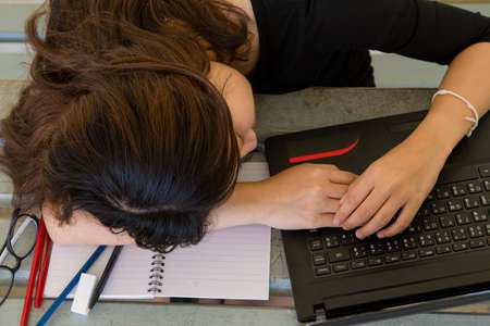 Young woman tired of working, doing homework, with notebook and laptopの写真素材