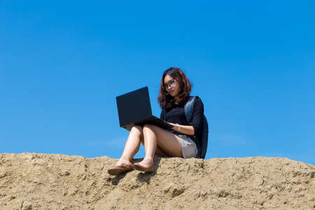 young woman working with laptop on the mountain with blue sky backgroundの写真素材