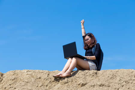 young woman working with laptop on the mountain with blue sky backgroundの写真素材