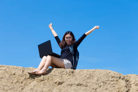 young woman working with laptop on the mountain with blue sky backgroundの写真素材