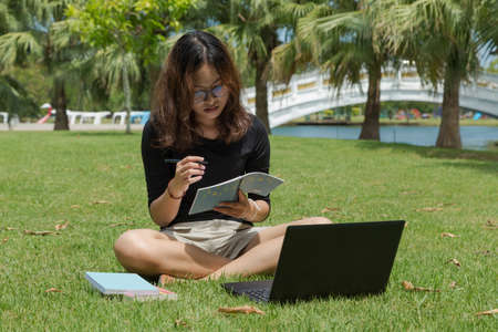 young woman working on laptop outdoors. image of female student working on laptop while sitting in a park with booksの写真素材