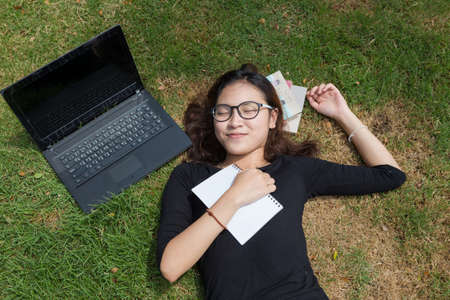 young woman working on laptop outdoors. image of female student working on laptop while lying on a grass in a park with booksの写真素材