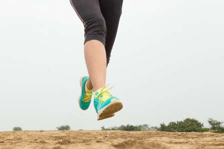 young woman running on mountain trail with white background, closeup on shoeの写真素材
