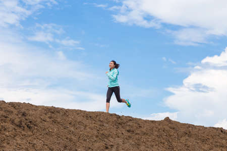 young woman running on trail with blue sky backgroundの写真素材