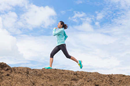young woman running on trail with blue sky backgroundの写真素材