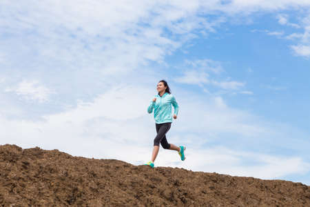 young woman running on trail with blue sky backgroundの写真素材