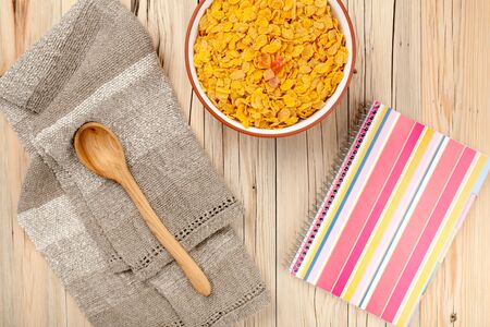 Cornflakes and notebook on wooden background