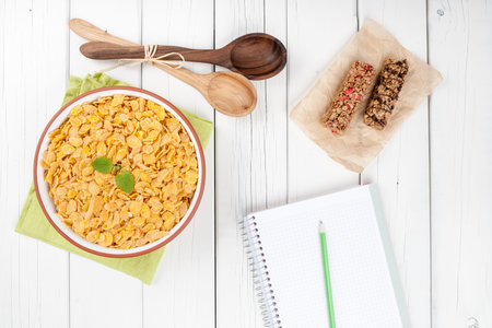Cornflakes muesli bars and notebook on wooden background