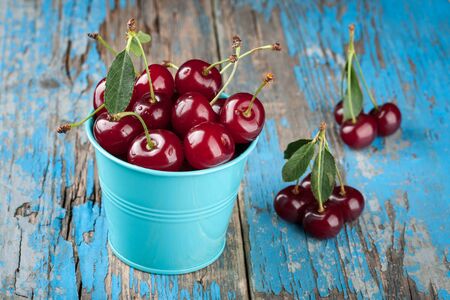 Ripe cherries in the blue bucket on wooden table close upの写真素材