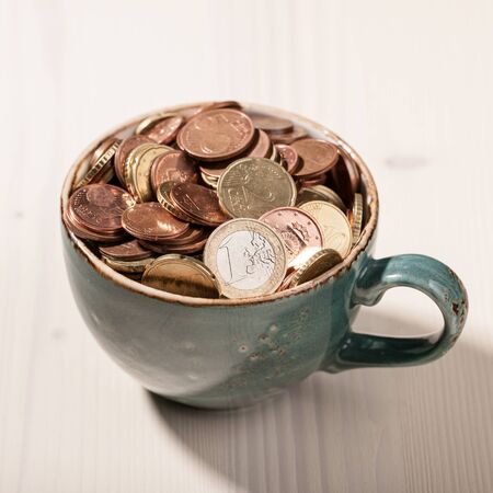 Euro coins in the ceramic cup on wooden tableの写真素材