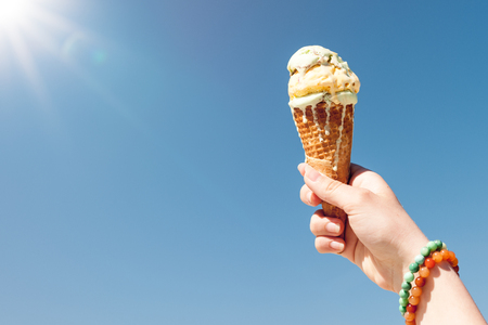 Hand holding ice cream cone on the sky background