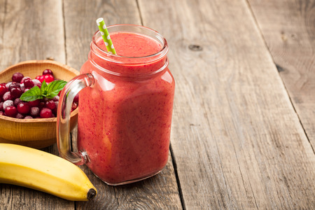 Banana-cranberry smoothie mug and ingredients on wooden tableの写真素材
