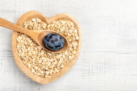 Dry oat flakes and plum in heart shaped wooden bowlの写真素材