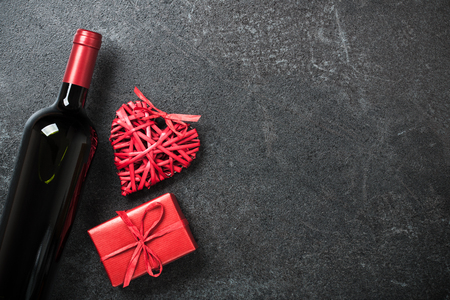 Red wine bottle, gift box and wicker heart on black backgroundの写真素材