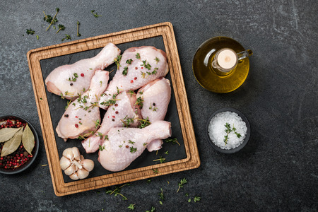 Raw chicken legs on cutting board and spices on blackboardの写真素材
