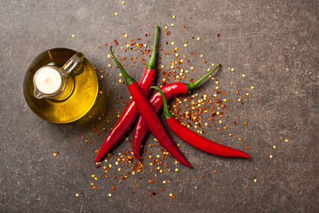 Red chili pepper and pitcher of oil on stone backgroundの写真素材