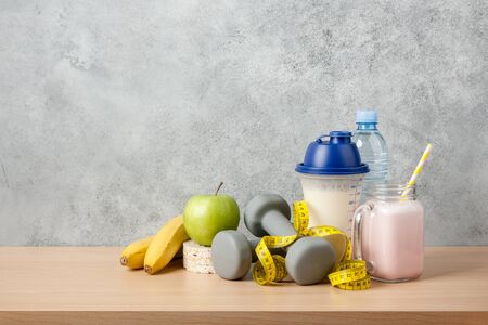 Protein cocktail, dumbbells, measuring tape, water bottle and fresh fruits on wooden tableの写真素材