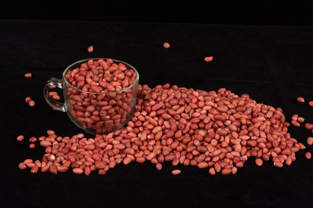 Pile of raw peanuts in a glass cup on a black background