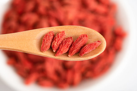 Dried goji berries in a wooden spoon on a white background