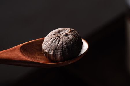 A round brown object in a wooden spoon on a black surface.の写真素材