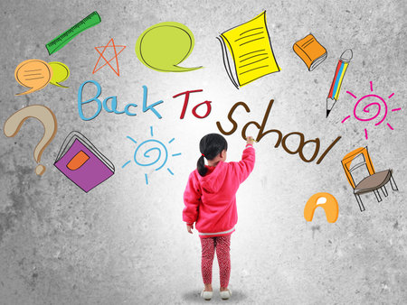 Little girl writing back to school text on wall 
