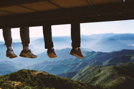 two men legs hanging from the bench against a blue sky and mountains view.                                の写真素材