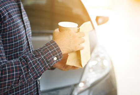 Man holding cup coffee and bread in paper bag.                                              の写真素材