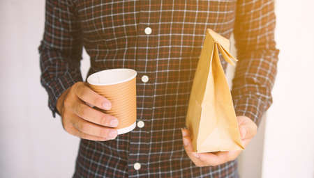 Man holding cup coffee and bread in paper bag.                                 の写真素材