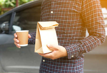 Man holding cup coffee and bread in paper bag.                                 の写真素材