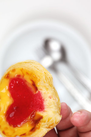 Hand pick egg tart have red heart shape on white plate with spoon and folk background 
