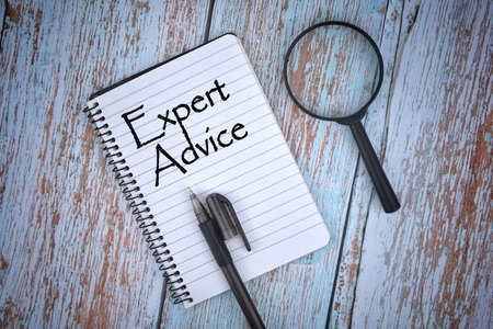 Selective focus image of magnifying glass with a pen on a wooden background with Expert Advice wording . Vintage style. Business and economy concept.の写真素材