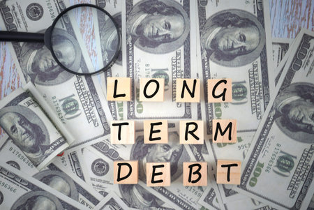 Magnifying glass with bank note dollar on a ground with LONG TERM DEBT wording on a wooden block....