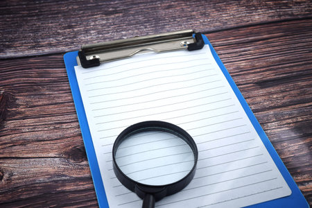 An image of magnifying glass with a paper on file holder. Blank space for business and education...
