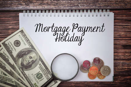 Selective focus image bank note,magnifying glass and coin with Mortgage Payment Holiday wording on a wooden backgroundの写真素材