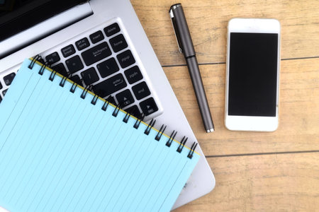 Selective focus image of laptop,pen,phone and book with copy space on wooden background