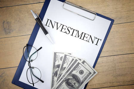 INVESTMENT wording with selective focus of bank note,pen, file holder and spectacles on wooden background. Business and economy conceptの写真素材