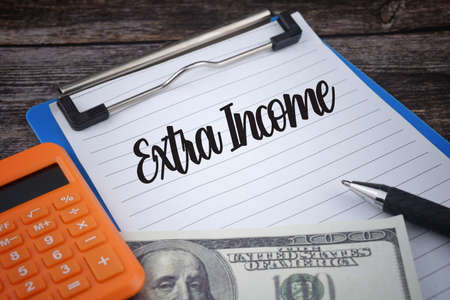 Extra income wording with calculator, bank note and pen on wooden background. Economy conceptの写真素材
