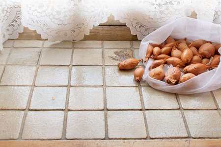 Burlap sack bags with shallot onions from local market, view from above and isolated on light tiles. Eco bagの写真素材