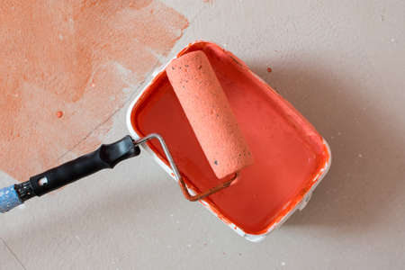 concrete floor with protection layer, orange background with structure, protective orange paint, detail on a bucket with paint and with a rollerの写真素材
