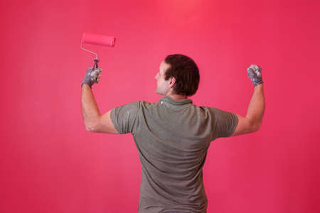 A man paints the wall with pink paint, a view from the back, holding a paint roller, strong handsome manの写真素材