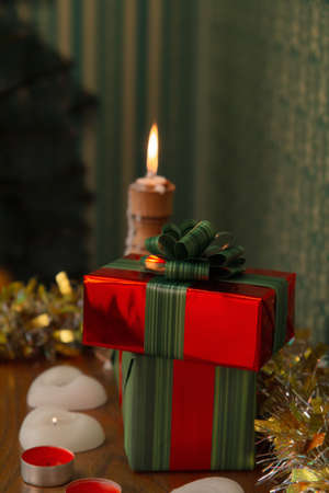New Year's gifts in red packaging lie on a shelf with candles, in the background a candle is burning and there is a Christmas treeの写真素材
