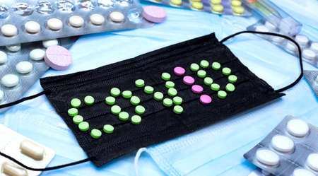 The inscription COVID from green and pink pills on the background of a black mask, flatlay
