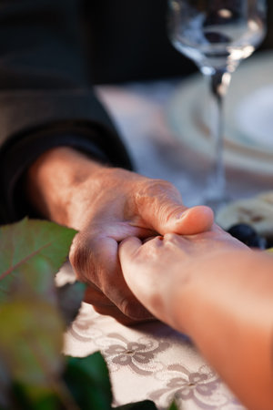 old man and woman hold hands at a romantic dinner at a restaurant on Valentine's Day, close-upの写真素材