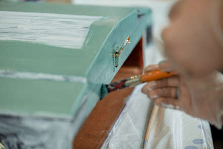 Womens hands paint a wooden retro box with a brush in green, furniture restoration