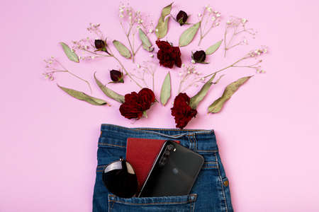 On a pink background, a layout of flowers, passport, mobile phone and sunglasses peeking out of the pocket of jeansの写真素材