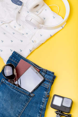 Action camera, sunglasses and passport lie on summer clothes on a yellow background